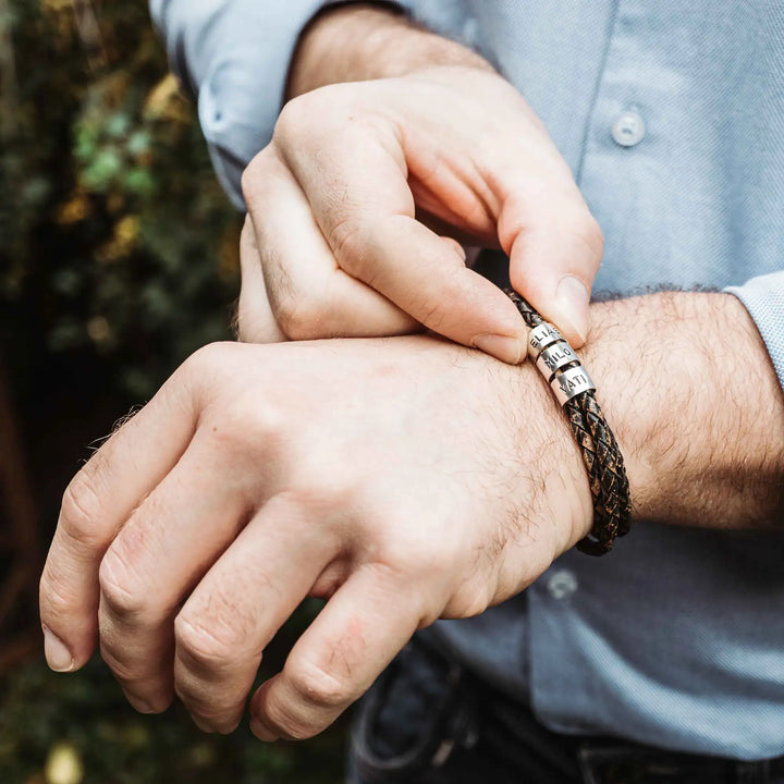 Ein geflochtenes Armband für Herren aus rustikalem, braun-schwarzen Leder im Wickelarmband Look, personalisiert mit Namen Gravur auf Sterling Silber 925 Perlen. Das Armband lässt sich mit einem Karabiner aus Edelstahl verschließen.