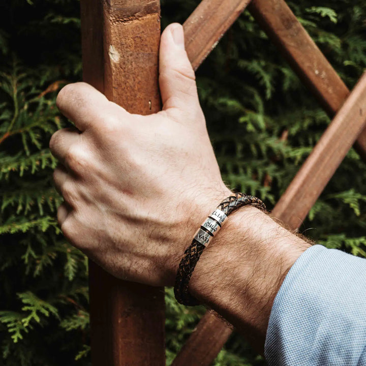 Ein geflochtenes Armband für Herren aus rustikalem, braun-schwarzen Leder im Wickelarmband Look, personalisiert mit Namen Gravur auf Sterling Silber 925 Perlen. Das Armband lässt sich mit einem Karabiner aus Edelstahl verschließen.