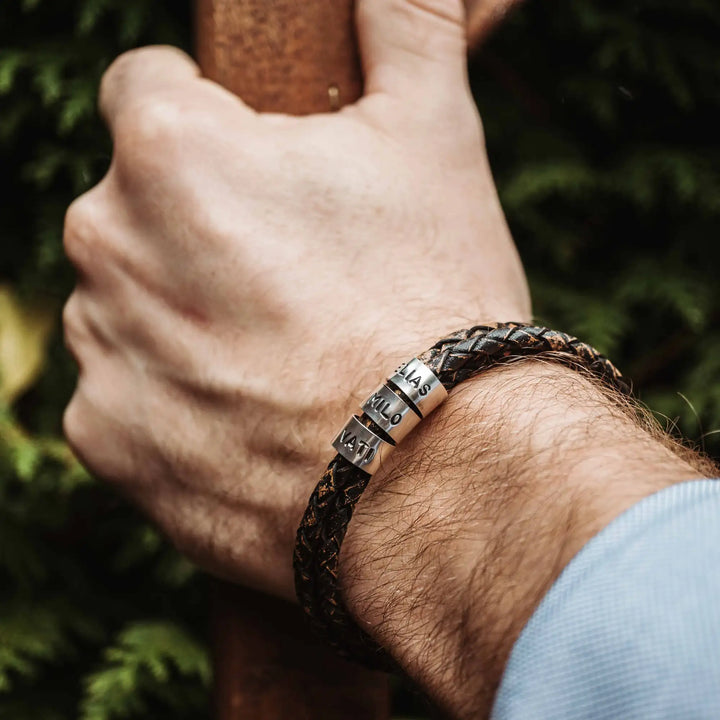 Ein geflochtenes Armband für Herren aus rustikalem, braun-schwarzen Leder im Wickelarmband Look, personalisiert mit Namen Gravur auf Sterling Silber 925 Perlen. Das Armband lässt sich mit einem Karabiner aus Edelstahl verschließen.