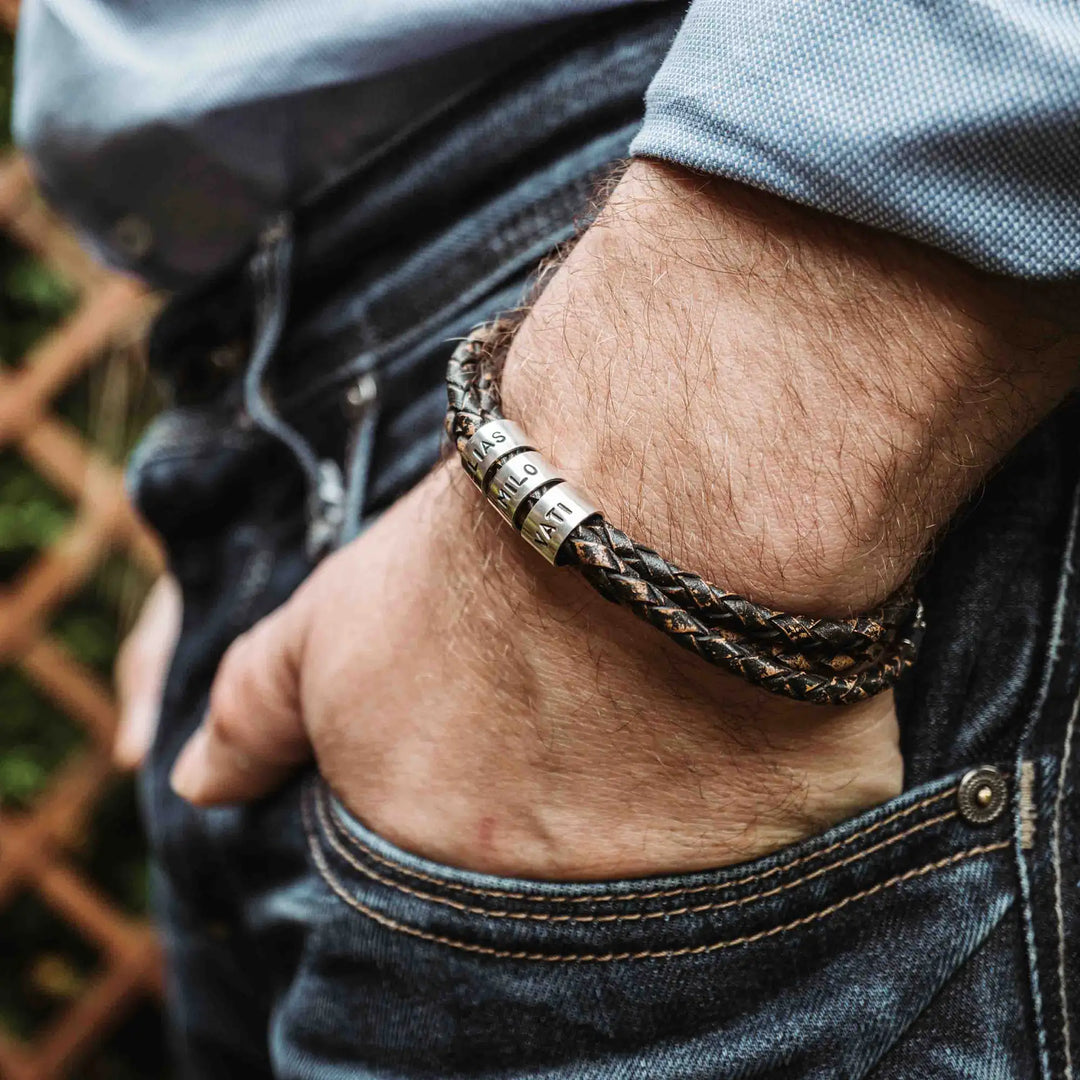 Ein geflochtenes Armband für Herren aus rustikalem, braun-schwarzen Leder im Wickelarmband Look, personalisiert mit Namen Gravur auf Sterling Silber 925 Perlen. Das Armband lässt sich mit einem Karabiner aus Edelstahl verschließen.