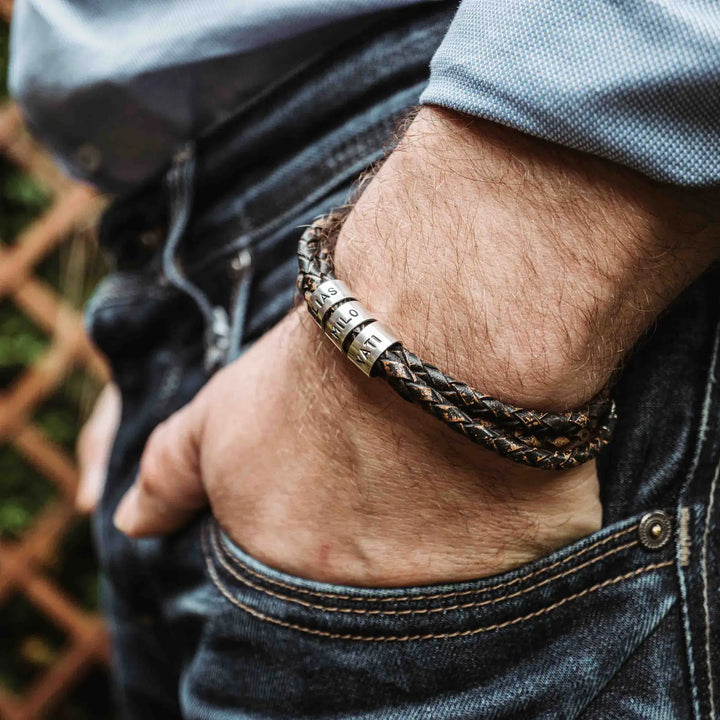 Ein geflochtenes Armband für Herren aus rustikalem, braun-schwarzen Leder im Wickelarmband Look, personalisiert mit Namen Gravur auf Sterling Silber 925 Perlen. Das Armband lässt sich mit einem Karabiner aus Edelstahl verschließen.