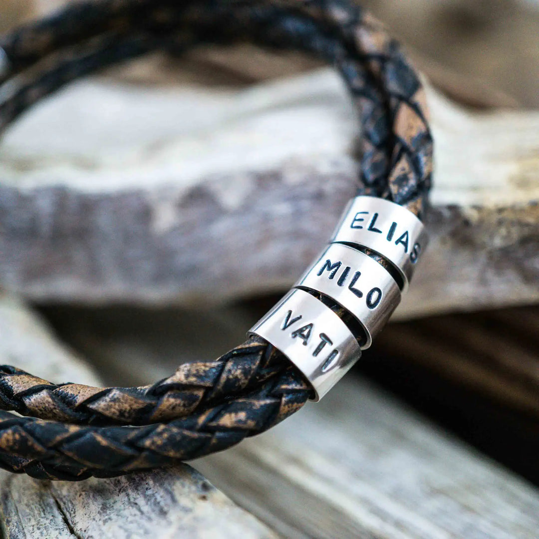 Ein geflochtenes Armband für Herren aus rustikalem, braun-schwarzen Leder im Wickelarmband Look, personalisiert mit Namen Gravur auf Sterling Silber 925 Perlen. Das Armband lässt sich mit einem Karabiner aus Edelstahl verschließen.