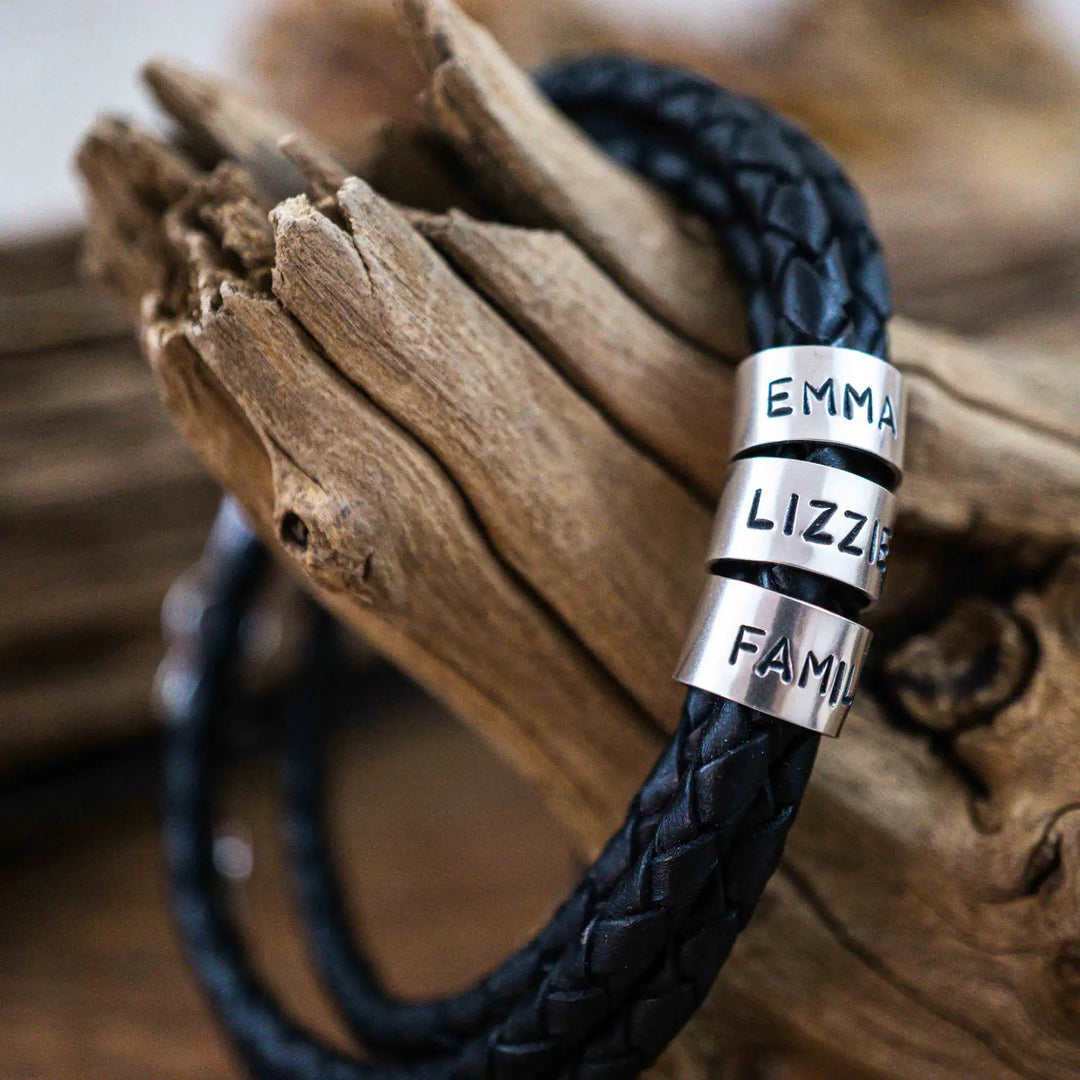 Ein geflochtenes Armband für Herren aus schwarzem Leder im Wickelarmband Look, personalisiert mit Gravur von Namen und Datum auf Sterling Silber 925 Perlen. Das Armband lässt sich mit einem Karabiner aus Edelstahl verschließen.