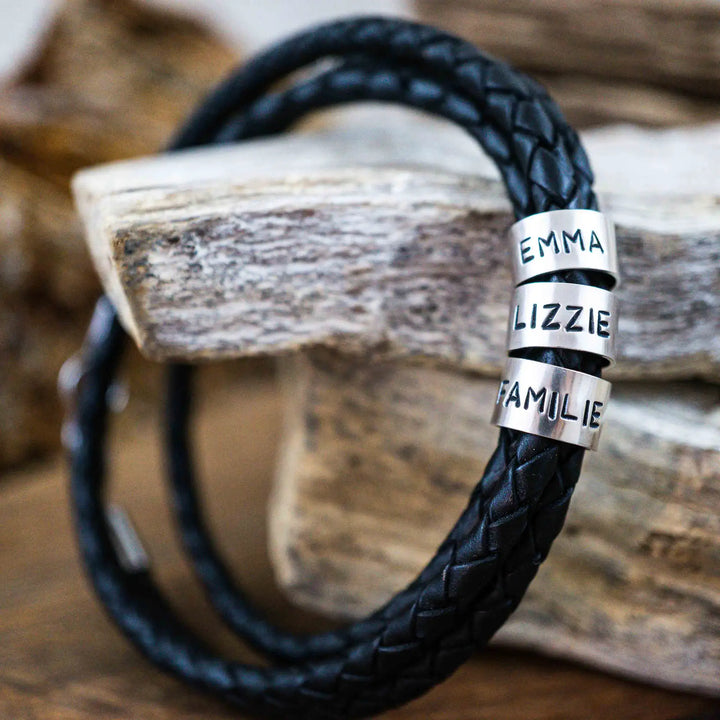 Ein geflochtenes Armband für Herren aus schwarzem Leder im Wickelarmband Look, personalisiert mit Gravur von Namen und Datum auf Sterling Silber 925 Perlen. Das Armband lässt sich mit einem Karabiner aus Edelstahl verschließen.