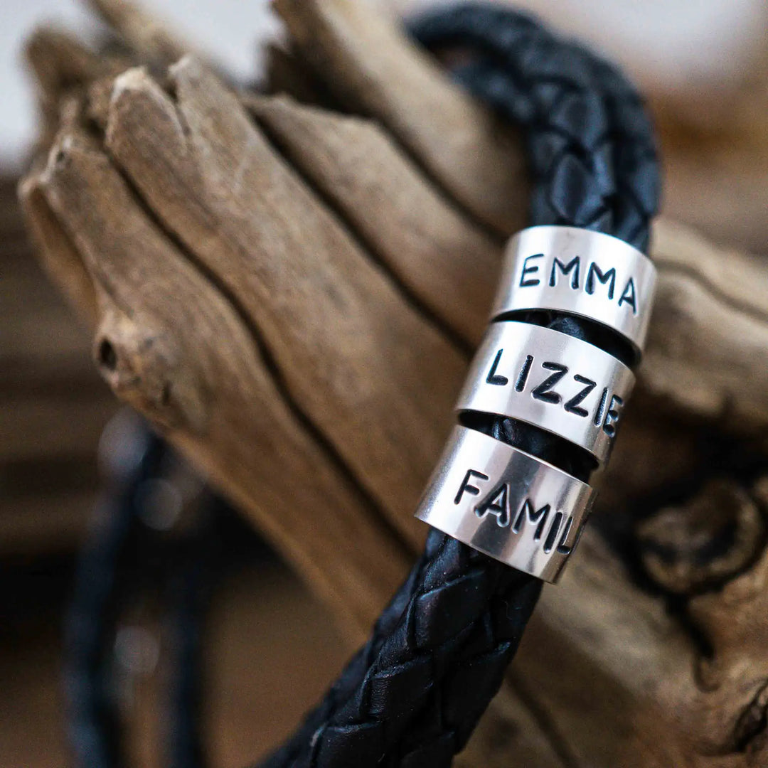 Ein geflochtenes Armband für Herren aus schwarzem Leder im Wickelarmband Look, personalisiert mit Gravur von Namen und Datum auf Sterling Silber 925 Perlen. Das Armband lässt sich mit einem Karabiner aus Edelstahl verschließen.