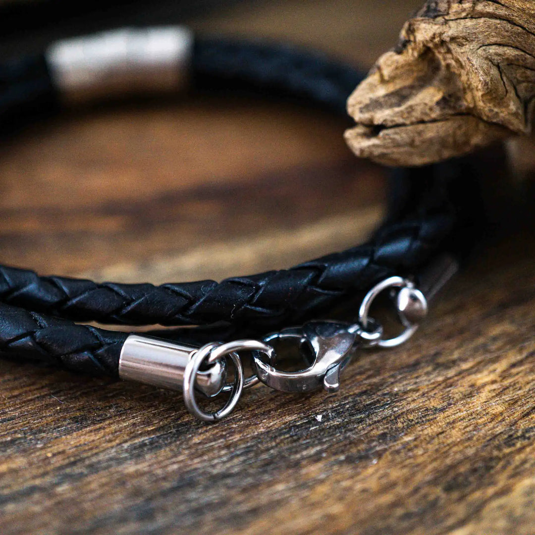 Ein geflochtenes Armband für Herren aus schwarzem Leder im Wickelarmband Look, personalisiert mit Gravur von Namen und Datum auf Sterling Silber 925 Perlen. Das Armband lässt sich mit einem Karabiner aus Edelstahl verschließen.