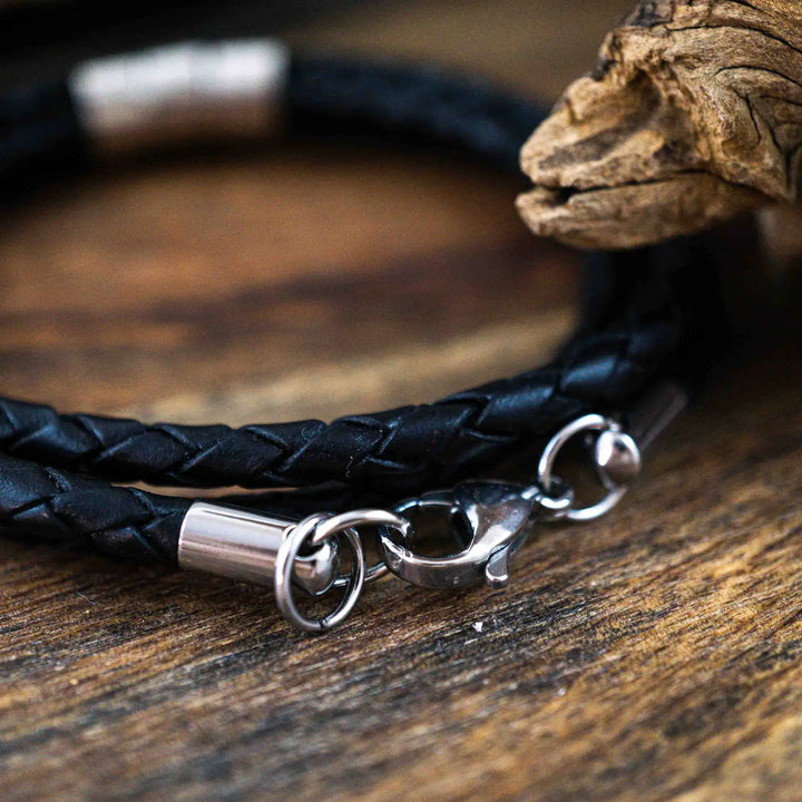 Ein geflochtenes Armband für Herren aus schwarzem Leder im Wickelarmband Look, personalisiert mit Gravur von Namen und Datum auf Sterling Silber 925 Perlen. Das Armband lässt sich mit einem Karabiner aus Edelstahl verschließen.