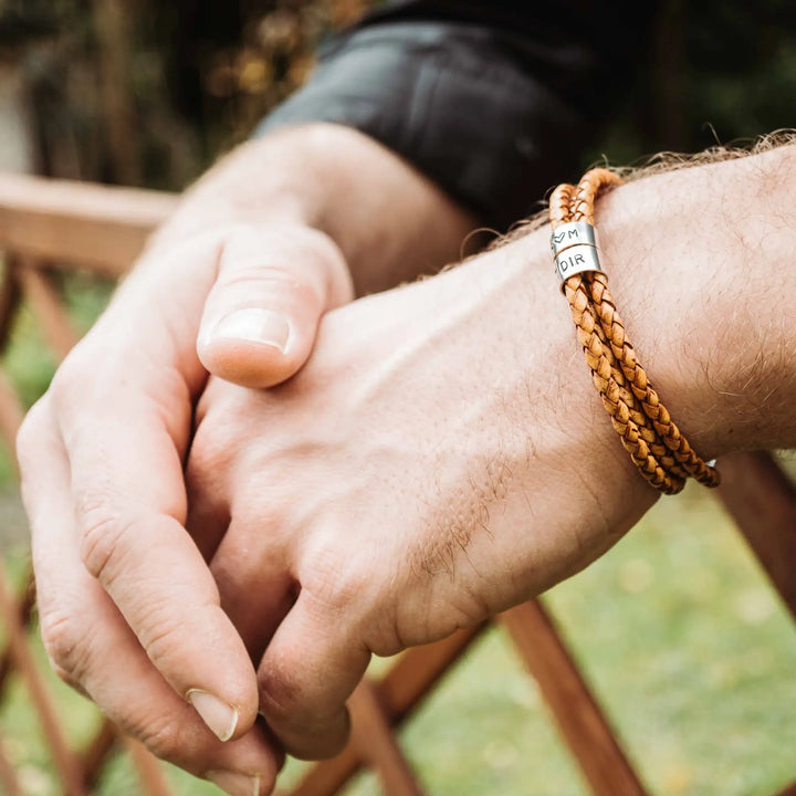 Ein geflochtenes Armband für Herren aus senfgelbem/hellbraunem Leder im Wickelarmband Look, personalisiert mit Namen und Datum Gravur auf Sterling Silber 925 Perlen. Das Armband lässt sich mit einem Karabiner aus Edelstahl verschließen.