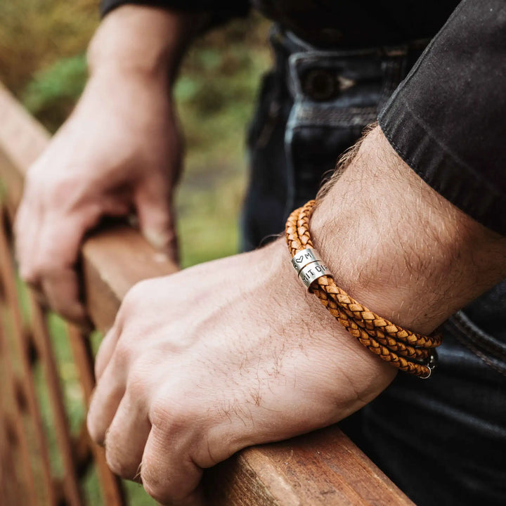Ein geflochtenes Armband für Herren aus senfgelbem/hellbraunem Leder im Wickelarmband Look, personalisiert mit Namen und Datum Gravur auf Sterling Silber 925 Perlen. Das Armband lässt sich mit einem Karabiner aus Edelstahl verschließen.