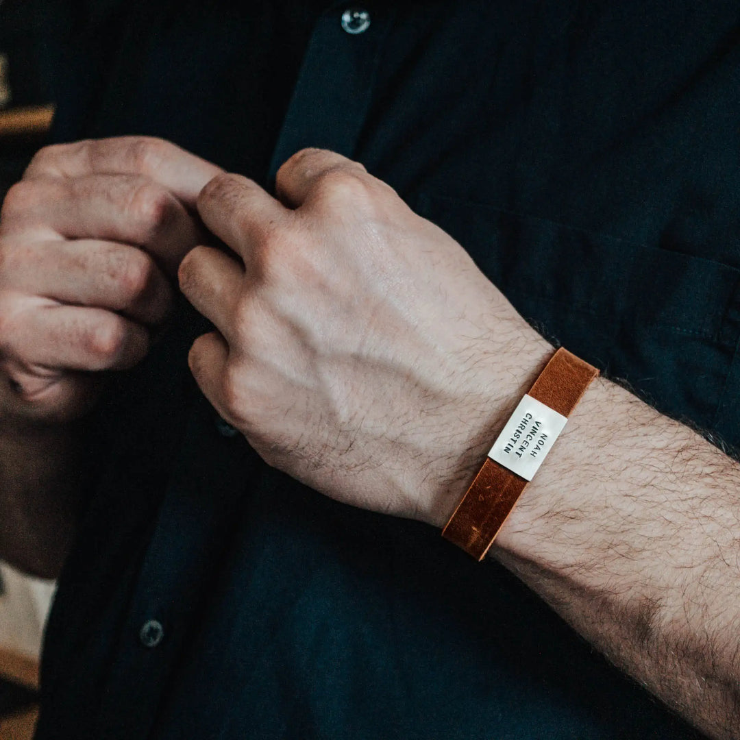 Ein breites, flaches Armband für Herren aus braunem Leder, personalisiert mit Gravur von Namen oder Datum auf einer großen, rechteckigen Sterling Silber 925 Perle. Das Armband lässt sich mit einem stabilen Verschluss aus Edelstahl verschließen und selbst auf die gewünschte Länge kürzen, was es zum perfekten Geschenk macht.