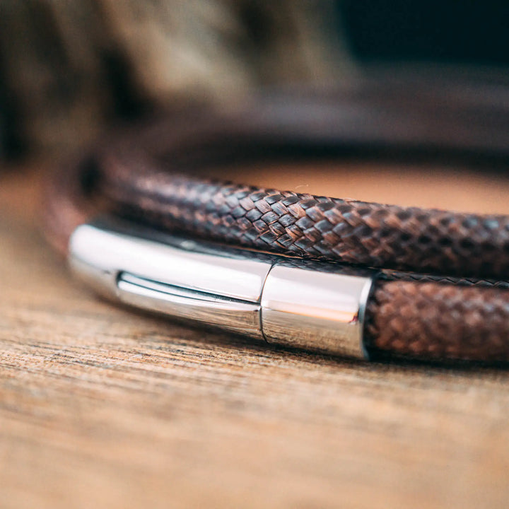 Ein veganes Armband aus braunem Synthetik/Baumwoll-Band im Wickelarmband Look, personalisiert mit Gravur von Namen oder Datum auf runden Sterling Silber 925 Perlen. Das Armband lässt sich mit einem stabilen Verschluss aus Edelstahl verschließen.