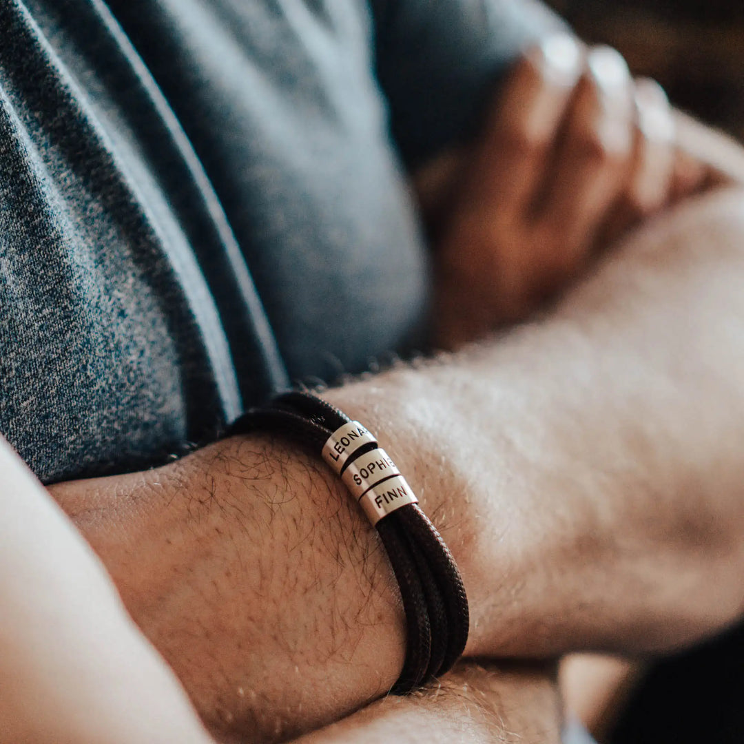 Ein veganes Armband aus braunem Synthetik/Baumwoll-Band im Wickelarmband Look, personalisiert mit Gravur von Namen oder Datum auf runden Sterling Silber 925 Perlen. Das Armband lässt sich mit einem stabilen Verschluss aus Edelstahl verschließen.