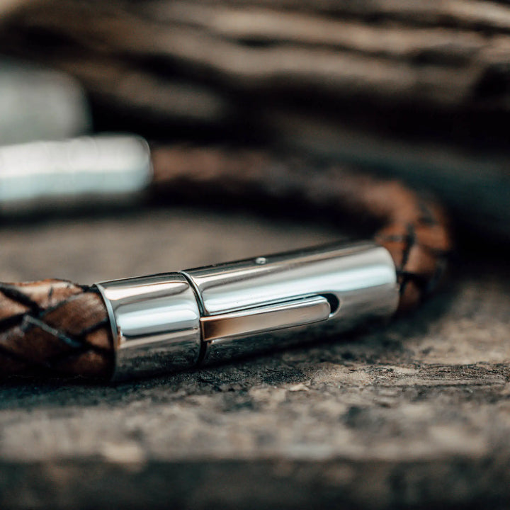 Ein dickes, geflochtenes Armband für Herren aus braunem Leder, personalisiert mit Gravur von Namen und Datum auf Sterling Silber 925 Perlen. Das Armband lässt sich mit einem stabilen Verschluss aus Edelstahl verschließen.
