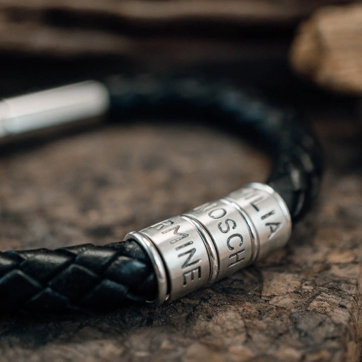 Ein dickes, geflochtenes Armband für Herren aus schwarzem Leder, personalisiert mit Gravur von Namen und Datum auf Sterling Silber 925 Perlen. Das Armband lässt sich mit einem stabilen Verschluss aus Edelstahl verschließen.
