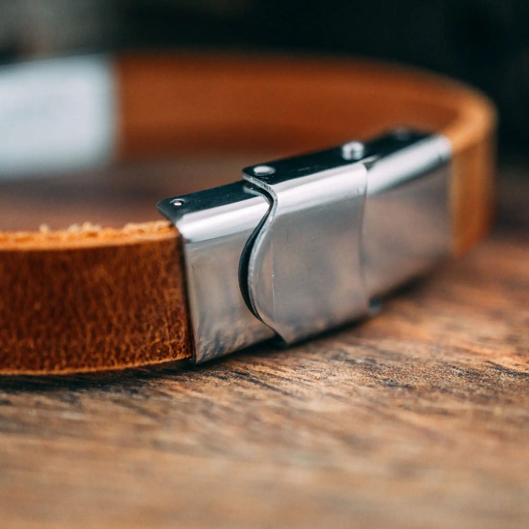 Ein schmales, flaches Armband für Herren aus braunem Leder, personalisiert mit Gravur von Namen oder Datum auf einer rechteckigen Sterling Silber 925 Perle. Das Armband lässt sich mit einem stabilen Verschluss aus Edelstahl verschließen und selbst auf die gewünschte Länge kürzen, was es zum perfekten Geschenk macht.