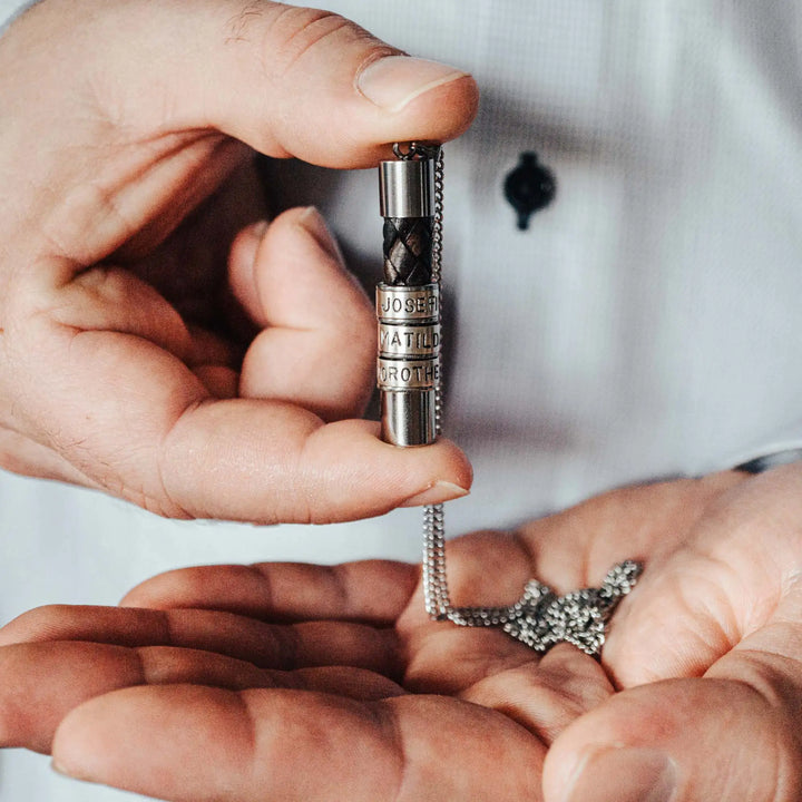 Eine Halskette für Männer aus braunem Leder-Anhänger und einer Edelstahl-Kette. Die Kette für Herren ist an dem zylindrischen Anhänger aus Leder personalisiert mit Gravur von Namen oder Datum auf zylindrischen Sterling Silber 925 Perlen. Die Kette lässt sich mit einem silbernen Karabiner aus Edelstahl verschließen.