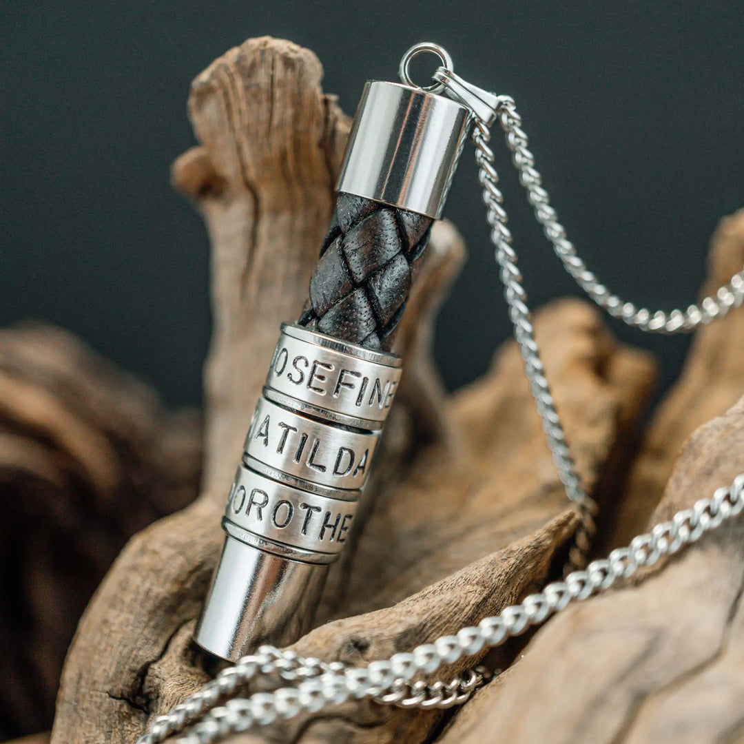 Eine Halskette für Männer aus braunem Leder-Anhänger und einer Edelstahl-Kette. Die Kette für Herren ist an dem zylindrischen Anhänger aus Leder personalisiert mit Gravur von Namen oder Datum auf zylindrischen Sterling Silber 925 Perlen. Die Kette lässt sich mit einem silbernen Karabiner aus Edelstahl verschließen.