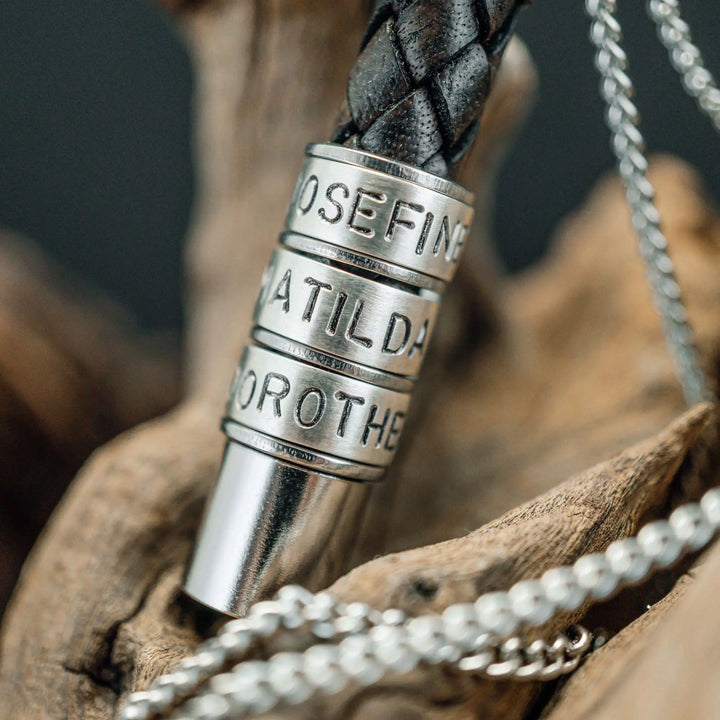 Eine Halskette für Männer aus braunem Leder-Anhänger und einer Edelstahl-Kette. Die Kette für Herren ist an dem zylindrischen Anhänger aus Leder personalisiert mit Gravur von Namen oder Datum auf zylindrischen Sterling Silber 925 Perlen. Die Kette lässt sich mit einem silbernen Karabiner aus Edelstahl verschließen.