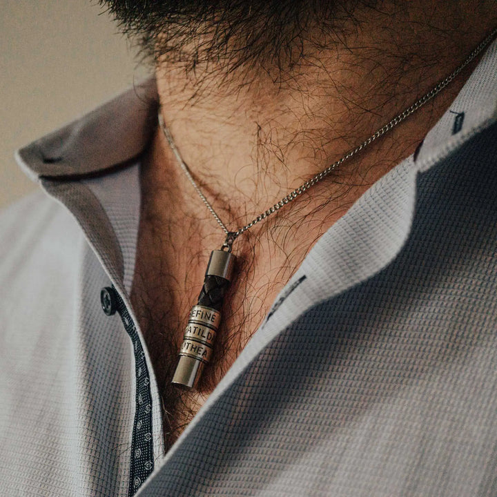 Eine Halskette für Männer aus braunem Leder-Anhänger und einer Edelstahl-Kette. Die Kette für Herren ist an dem zylindrischen Anhänger aus Leder personalisiert mit Gravur von Namen oder Datum auf zylindrischen Sterling Silber 925 Perlen. Die Kette lässt sich mit einem silbernen Karabiner aus Edelstahl verschließen.