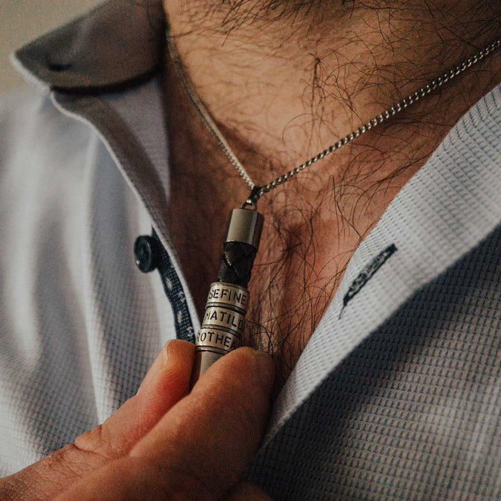 Eine Halskette für Männer aus braunem Leder-Anhänger und einer Edelstahl-Kette. Die Kette für Herren ist an dem zylindrischen Anhänger aus Leder personalisiert mit Gravur von Namen oder Datum auf zylindrischen Sterling Silber 925 Perlen. Die Kette lässt sich mit einem silbernen Karabiner aus Edelstahl verschließen.