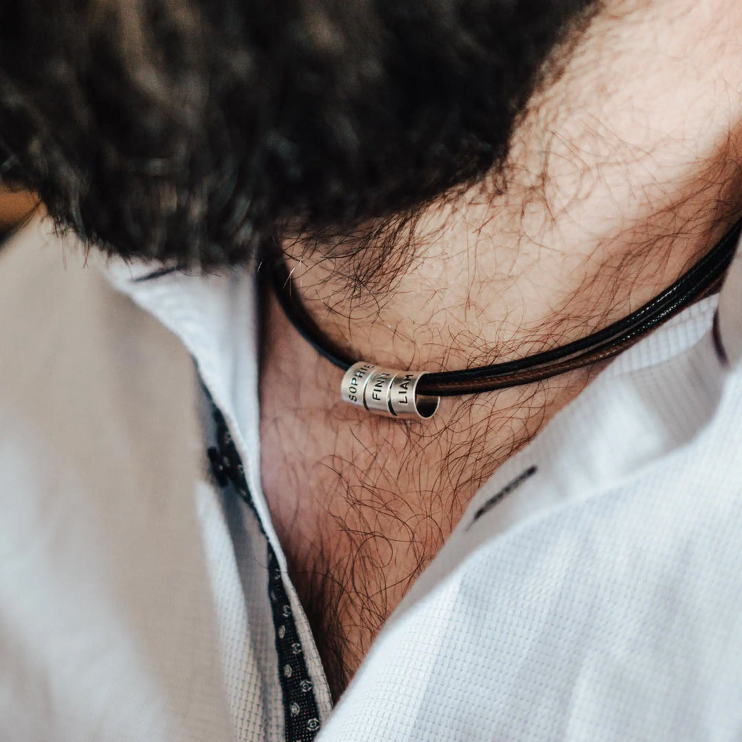 Eine vegane Halskette für Männer aus mehreren braunen und schwarzen Synthetik/Baumwoll-Bändern. Die Kette für Herren ist personalisiert mit Gravur von Namen oder Datum auf zylindrischen Sterling Silber 925 Perlen. Das Kette lässt sich mit einem stabilen Karabiner Verschluss aus Edelstahl verschließen.