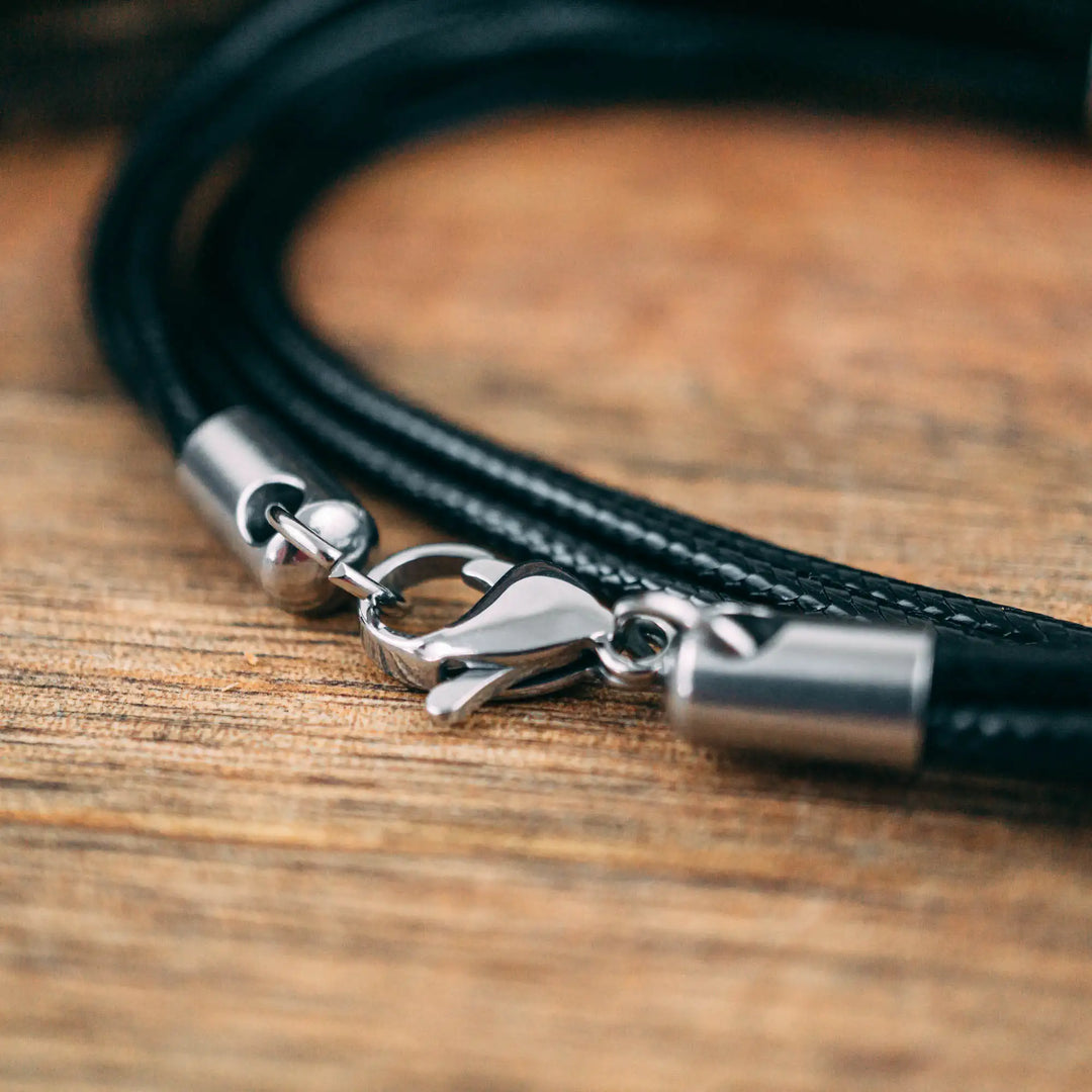 Eine vegane Halskette für Männer aus mehreren schwarzen Synthetik/Baumwoll-Bändern. Die Kette für Herren ist personalisiert mit Gravur von Namen oder Datum auf zylindrischen Sterling Silber 925 Perlen. Das Kette lässt sich mit einem stabilen Karabiner Verschluss aus Edelstahl verschließen.