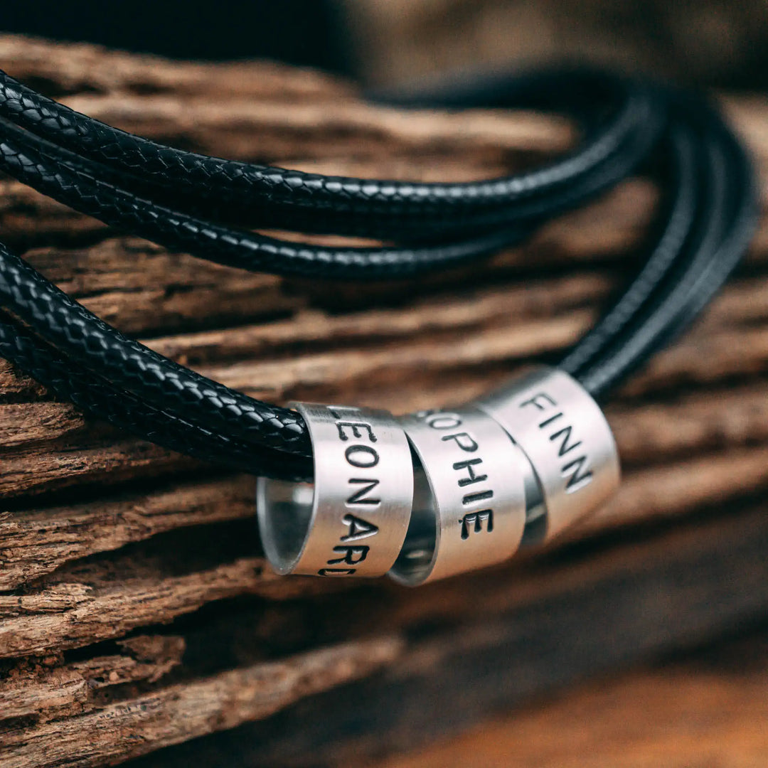 Eine vegane Halskette für Männer aus mehreren schwarzen Synthetik/Baumwoll-Bändern. Die Kette für Herren ist personalisiert mit Gravur von Namen oder Datum auf zylindrischen Sterling Silber 925 Perlen. Das Kette lässt sich mit einem stabilen Karabiner Verschluss aus Edelstahl verschließen.