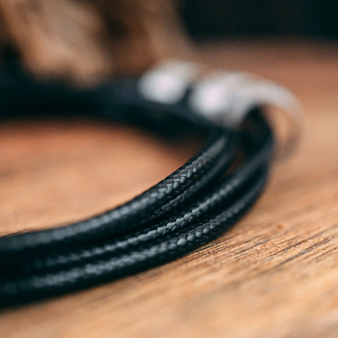 Eine vegane Halskette für Männer aus mehreren schwarzen Synthetik/Baumwoll-Bändern. Die Kette für Herren ist personalisiert mit Gravur von Namen oder Datum auf zylindrischen Sterling Silber 925 Perlen. Das Kette lässt sich mit einem stabilen Karabiner Verschluss aus Edelstahl verschließen.