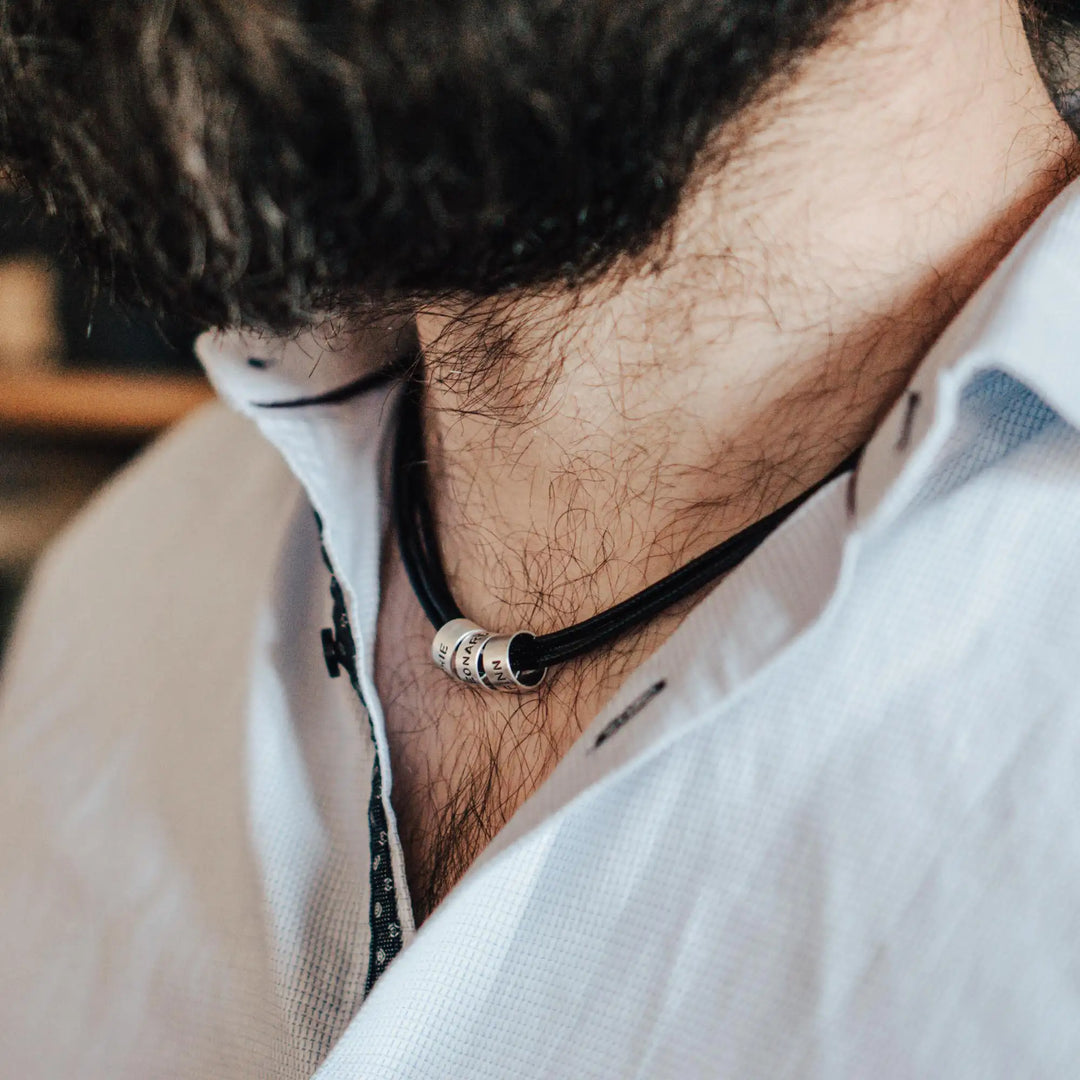 Eine vegane Halskette für Männer aus mehreren schwarzen Synthetik/Baumwoll-Bändern. Die Kette für Herren ist personalisiert mit Gravur von Namen oder Datum auf zylindrischen Sterling Silber 925 Perlen. Das Kette lässt sich mit einem stabilen Karabiner Verschluss aus Edelstahl verschließen.