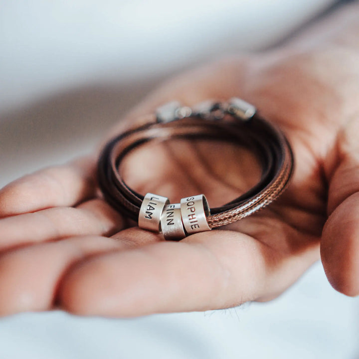 Eine vegane Halskette für Männer aus mehreren braunen Synthetik/Baumwoll-Bändern. Die Kette für Herren ist personalisiert mit Gravur von Namen oder Datum auf zylindrischen Sterling Silber 925 Perlen. Das Kette lässt sich mit einem stabilen Karabiner Verschluss aus Edelstahl verschließen.