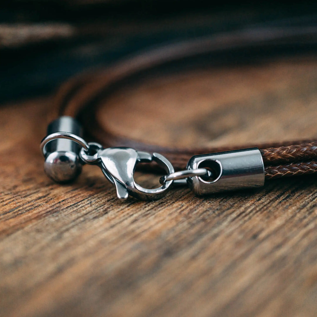 Eine vegane Halskette für Männer aus mehreren braunen Synthetik/Baumwoll-Bändern. Die Kette für Herren ist personalisiert mit Gravur von Namen oder Datum auf zylindrischen Sterling Silber 925 Perlen. Das Kette lässt sich mit einem stabilen Karabiner Verschluss aus Edelstahl verschließen.