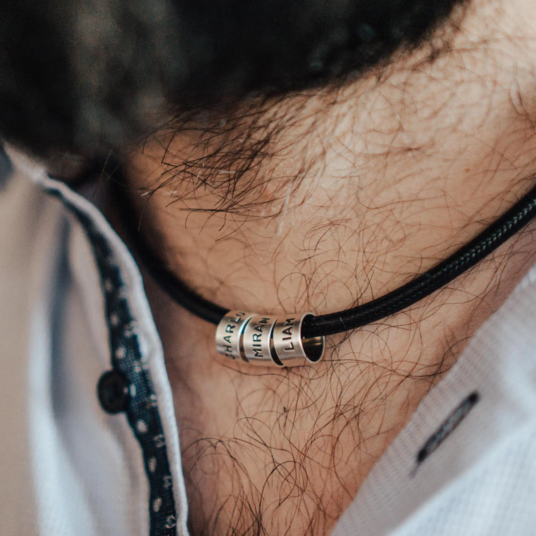 Eine vegane Halskette für Männer aus schwarzem Synthetik/Baumwoll-Band. Die Kette für Herren ist personalisiert mit Gravur von Namen oder Datum auf zylindrischen Sterling Silber 925 Perlen. Das Kette lässt sich mit einem stabilen Karabiner Verschluss aus Edelstahl verschließen.