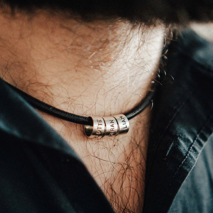 Eine vegane Halskette für Männer aus schwarzem Synthetik/Baumwoll-Band. Die Kette für Herren ist personalisiert mit Gravur von Namen oder Datum auf zylindrischen Sterling Silber 925 Perlen. Das Kette lässt sich mit einem stabilen Karabiner Verschluss aus Edelstahl verschließen.