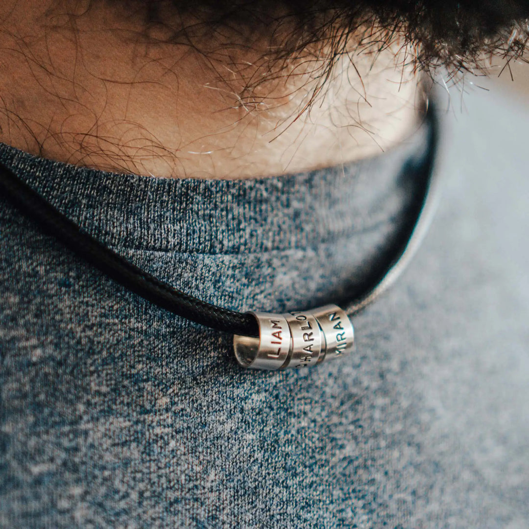 Eine vegane Halskette für Männer aus schwarzem Synthetik/Baumwoll-Band. Die Kette für Herren ist personalisiert mit Gravur von Namen oder Datum auf zylindrischen Sterling Silber 925 Perlen. Das Kette lässt sich mit einem stabilen Karabiner Verschluss aus Edelstahl verschließen.