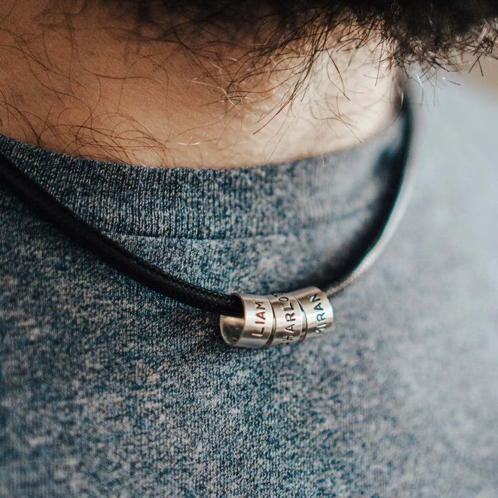 Eine vegane Halskette für Männer aus schwarzem Synthetik/Baumwoll-Band. Die Kette für Herren ist personalisiert mit Gravur von Namen oder Datum auf zylindrischen Sterling Silber 925 Perlen. Das Kette lässt sich mit einem stabilen Karabiner Verschluss aus Edelstahl verschließen.