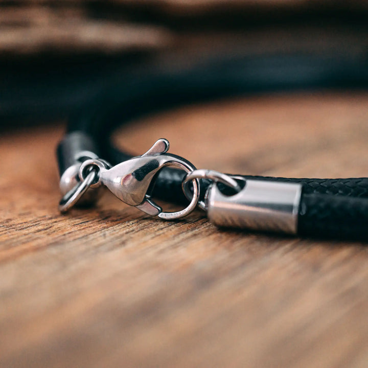 Eine vegane Halskette für Männer aus schwarzem Synthetik/Baumwoll-Band. Die Kette für Herren ist personalisiert mit Gravur von Namen oder Datum auf zylindrischen Sterling Silber 925 Perlen. Das Kette lässt sich mit einem stabilen Karabiner Verschluss aus Edelstahl verschließen.
