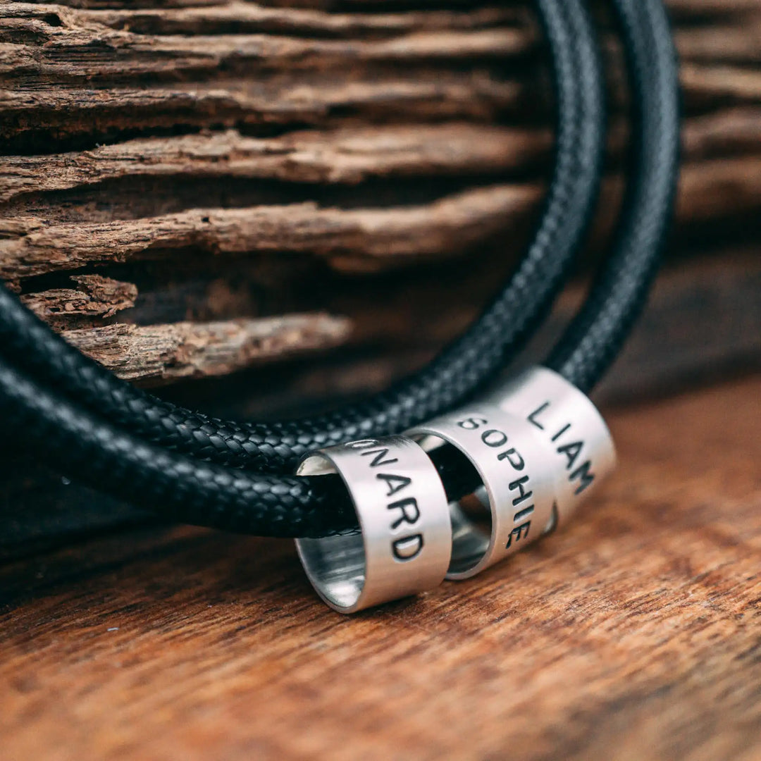Eine vegane Halskette für Männer aus schwarzem Synthetik/Baumwoll-Band. Die Kette für Herren ist personalisiert mit Gravur von Namen oder Datum auf zylindrischen Sterling Silber 925 Perlen. Das Kette lässt sich mit einem stabilen Karabiner Verschluss aus Edelstahl verschließen.
