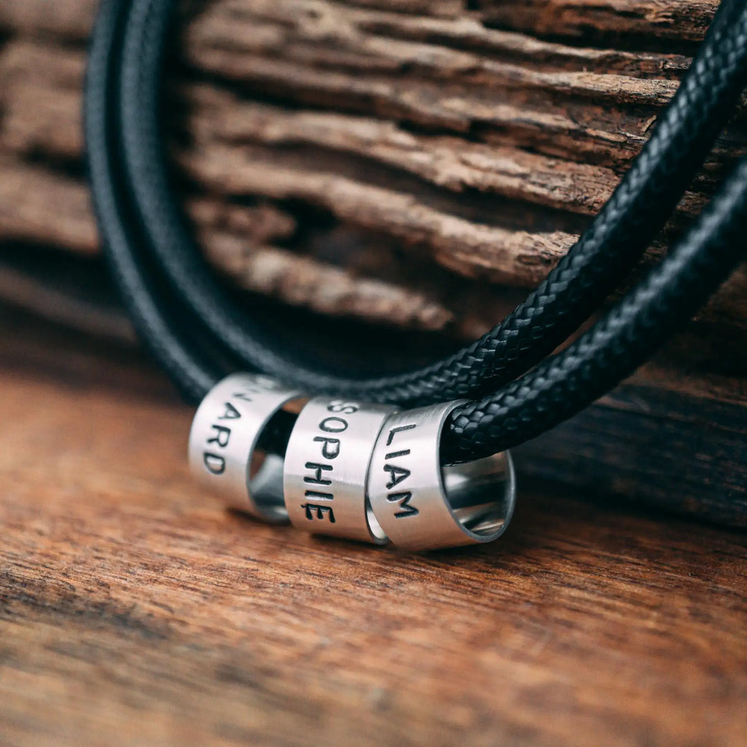 Eine vegane Halskette für Männer aus schwarzem Synthetik/Baumwoll-Band. Die Kette für Herren ist personalisiert mit Gravur von Namen oder Datum auf zylindrischen Sterling Silber 925 Perlen. Das Kette lässt sich mit einem stabilen Karabiner Verschluss aus Edelstahl verschließen.