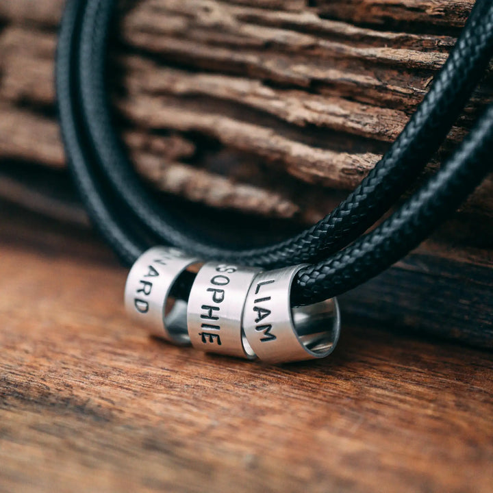 Eine vegane Halskette für Männer aus schwarzem Synthetik/Baumwoll-Band. Die Kette für Herren ist personalisiert mit Gravur von Namen oder Datum auf zylindrischen Sterling Silber 925 Perlen. Das Kette lässt sich mit einem stabilen Karabiner Verschluss aus Edelstahl verschließen.