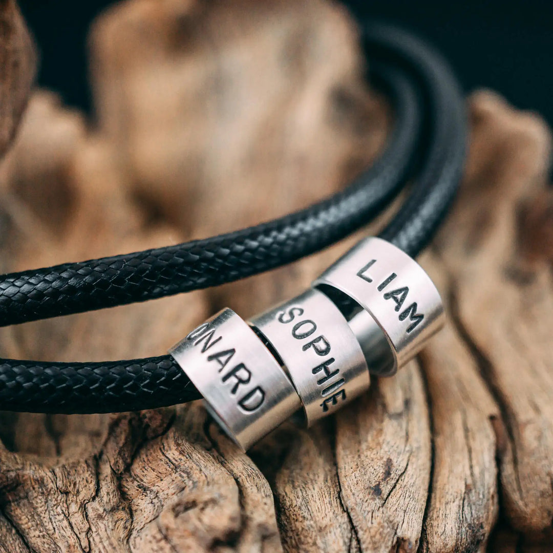 Eine vegane Halskette für Männer aus schwarzem Synthetik/Baumwoll-Band. Die Kette für Herren ist personalisiert mit Gravur von Namen oder Datum auf zylindrischen Sterling Silber 925 Perlen. Das Kette lässt sich mit einem stabilen Karabiner Verschluss aus Edelstahl verschließen.