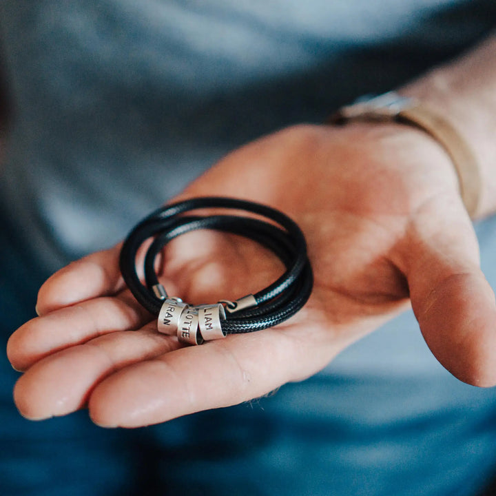 Eine vegane Halskette für Männer aus schwarzem Synthetik/Baumwoll-Band. Die Kette für Herren ist personalisiert mit Gravur von Namen oder Datum auf zylindrischen Sterling Silber 925 Perlen. Das Kette lässt sich mit einem stabilen Karabiner Verschluss aus Edelstahl verschließen.