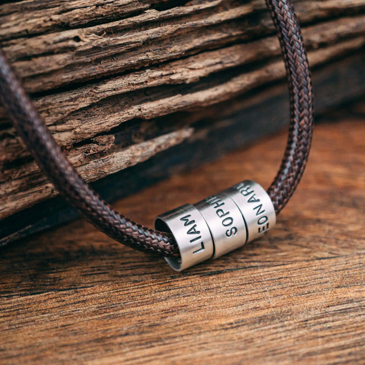 Eine vegane Halskette für Männer aus braunem Synthetik/Baumwoll-Band. Die Kette für Herren ist personalisiert mit Gravur von Namen oder Datum auf zylindrischen Sterling Silber 925 Perlen. Das Kette lässt sich mit einem stabilen Karabiner Verschluss aus Edelstahl verschließen.