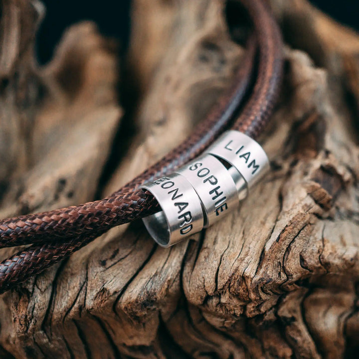 Eine vegane Halskette für Männer aus braunem Synthetik/Baumwoll-Band. Die Kette für Herren ist personalisiert mit Gravur von Namen oder Datum auf zylindrischen Sterling Silber 925 Perlen. Das Kette lässt sich mit einem stabilen Karabiner Verschluss aus Edelstahl verschließen.