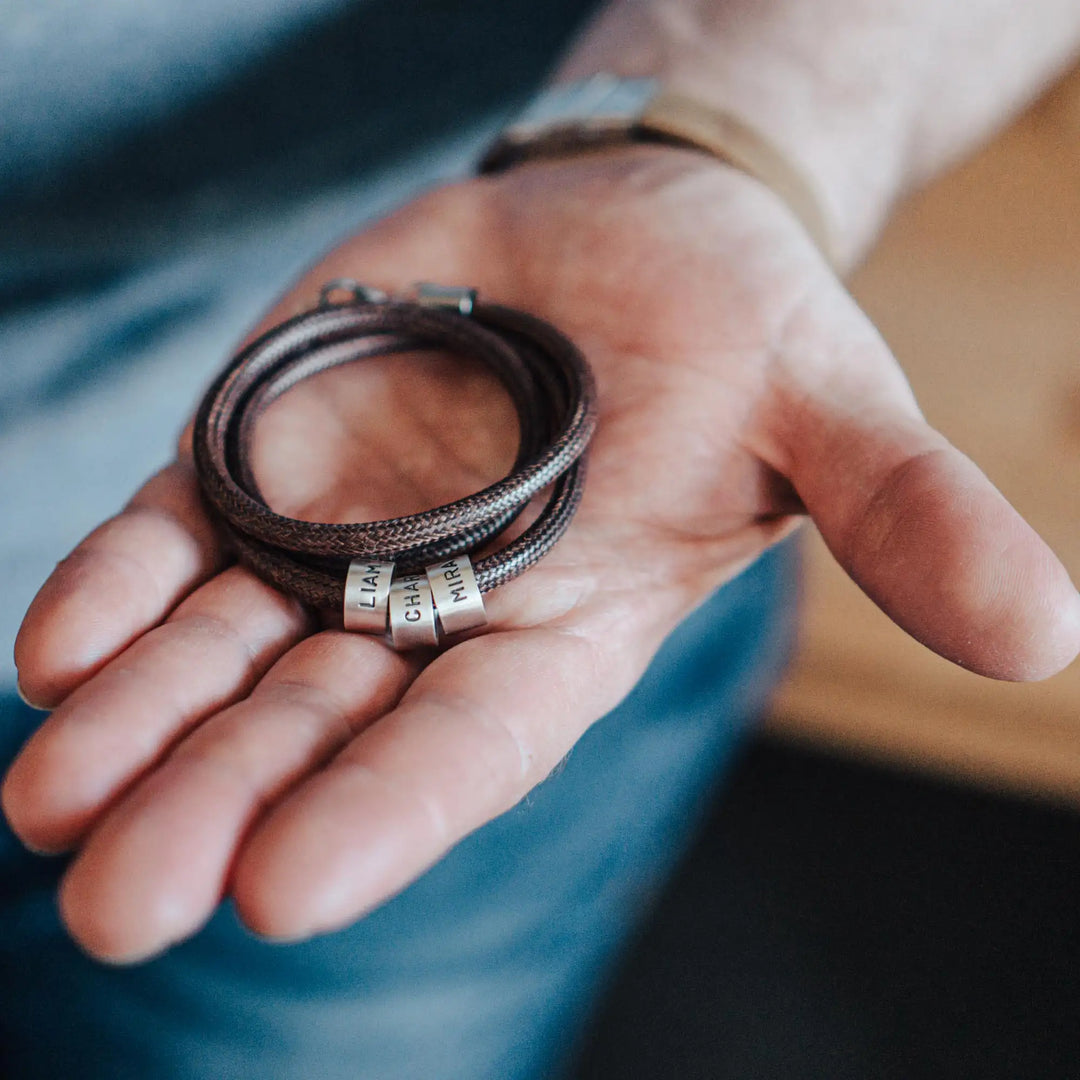 Eine vegane Halskette für Männer aus braunem Synthetik/Baumwoll-Band. Die Kette für Herren ist personalisiert mit Gravur von Namen oder Datum auf zylindrischen Sterling Silber 925 Perlen. Das Kette lässt sich mit einem stabilen Karabiner Verschluss aus Edelstahl verschließen.
