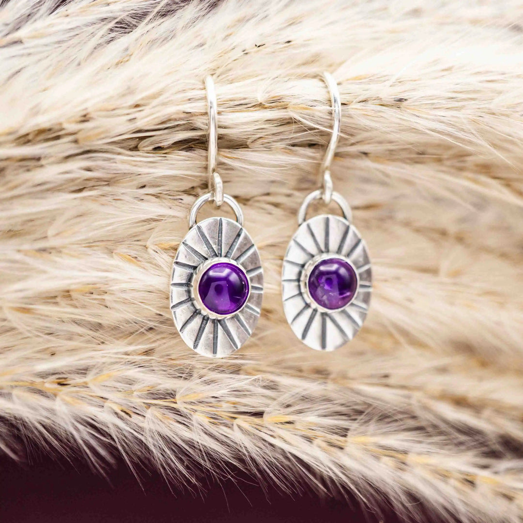 Silberohrringe mit Amethyst Cabochons auf getrocknetem Gras arrangiert