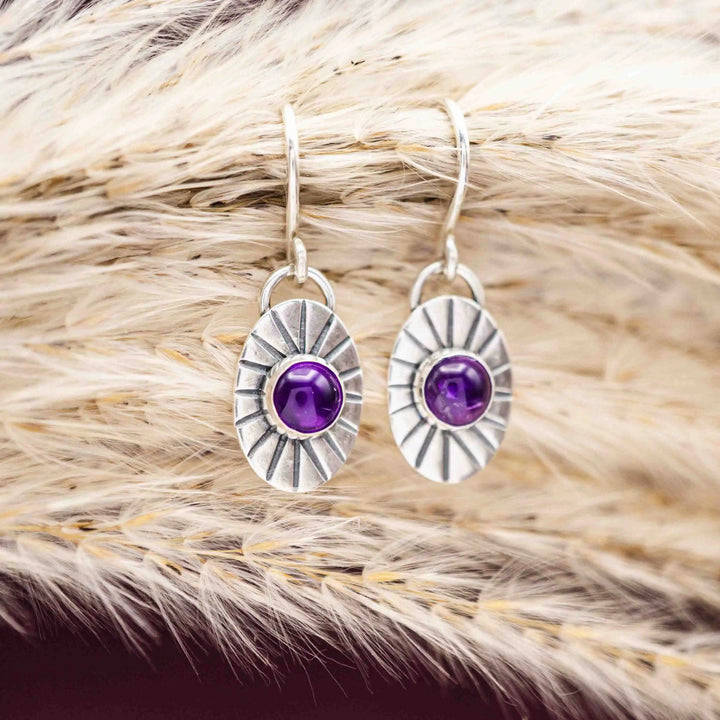 Silberohrringe mit Amethyst Cabochons auf getrocknetem Gras arrangiert