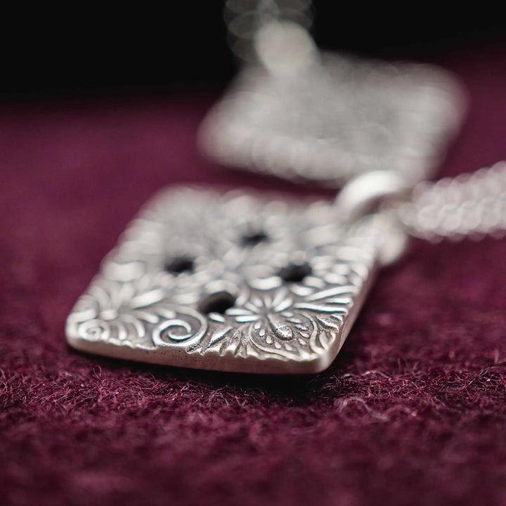 Freundschaftskette aus Silber 925 mit einem Knopf Anhänger an einer Kette. Der Knopf Anhänger ist eckig und mit einem floralen Muster versehen. Der eckige Knopf steht für Zusammenhalt, auch wenn nicht immer alles ganz "rund" läuft.