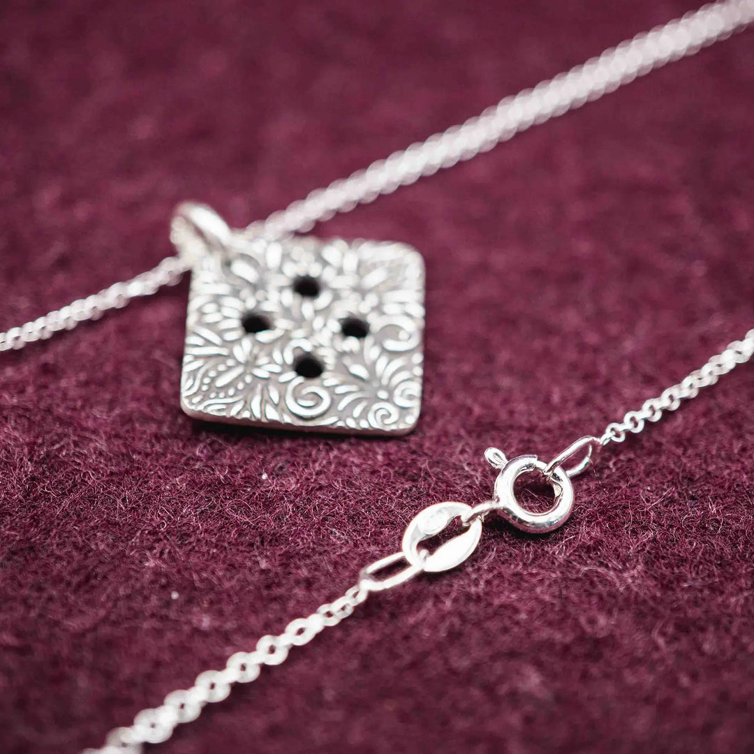 Freundschaftskette aus Silber 925 mit einem Knopf Anhänger an einer Kette. Der Knopf Anhänger ist eckig und mit einem floralen Muster versehen. Der eckige Knopf steht für Zusammenhalt, auch wenn nicht immer alles ganz "rund" läuft.