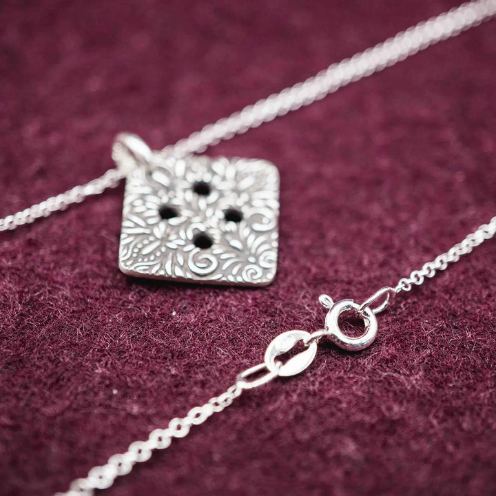 Freundschaftskette aus Silber 925 mit einem Knopf Anhänger an einer Kette. Der Knopf Anhänger ist eckig und mit einem floralen Muster versehen. Der eckige Knopf steht für Zusammenhalt, auch wenn nicht immer alles ganz "rund" läuft.