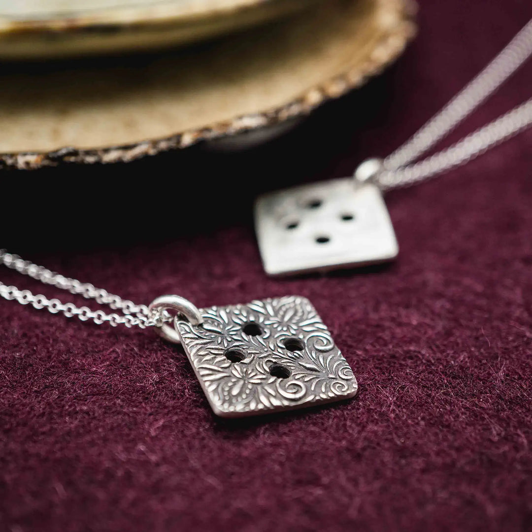 Freundschaftskette aus Silber 925 mit einem Knopf Anhänger an einer Kette. Der Knopf Anhänger ist eckig und mit einem floralen Muster versehen. Der eckige Knopf steht für Zusammenhalt, auch wenn nicht immer alles ganz "rund" läuft.